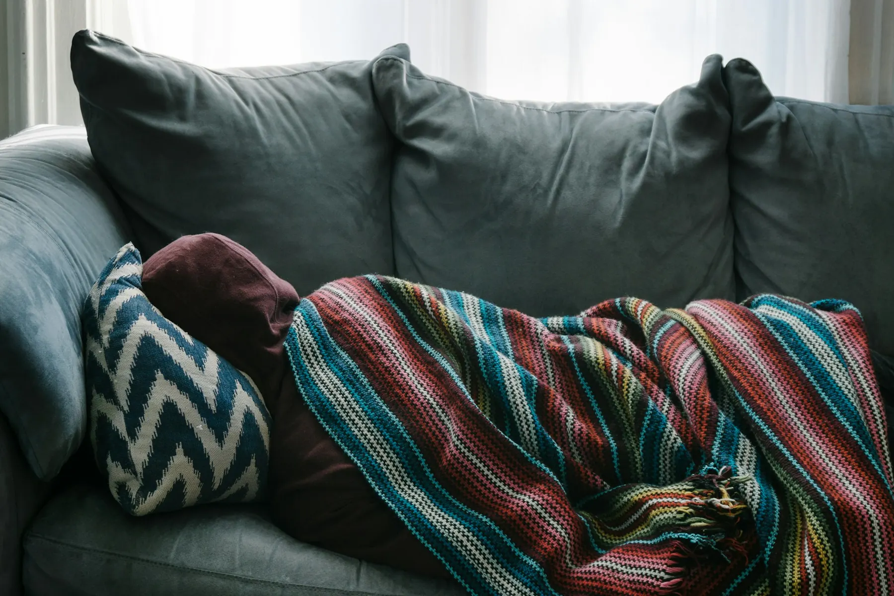 Jemand liegt eingepackt in eine Decke auf dem Sofa